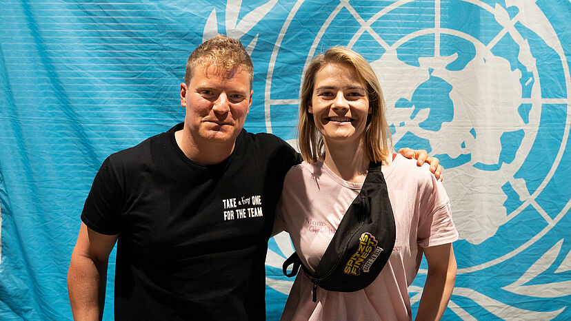 Thomas Spitzer und Hazel Brugger vor dem Logo der Vereinten Nationen